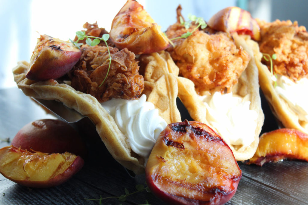 A close up shot of fried chicken and waffle tacos with grilled peaches