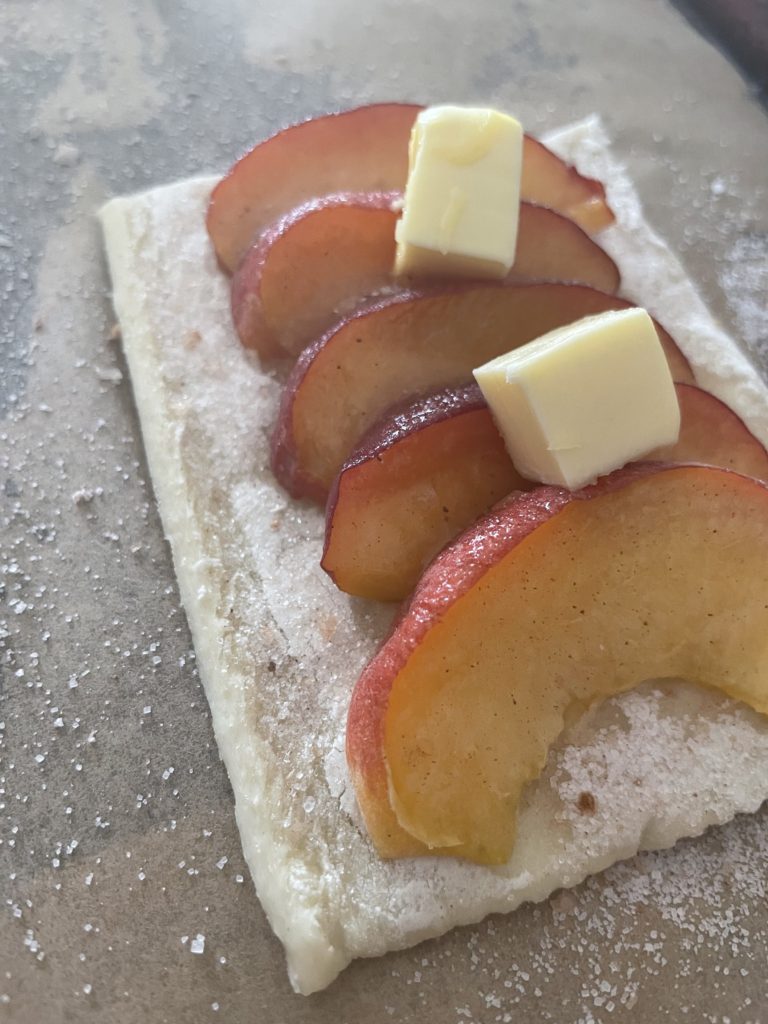 A close up of one piece of dough with peaches and butter on top
