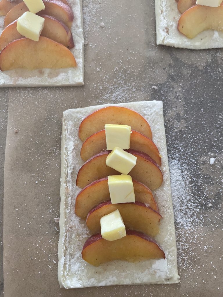 A close up of a piece of dough with sliced peaches, and butter on top