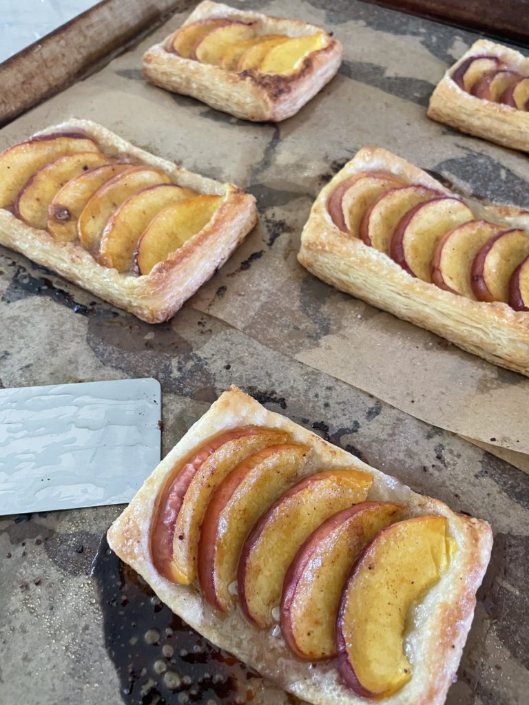 A sheet pan full of pastries with peaches on top and a spatula